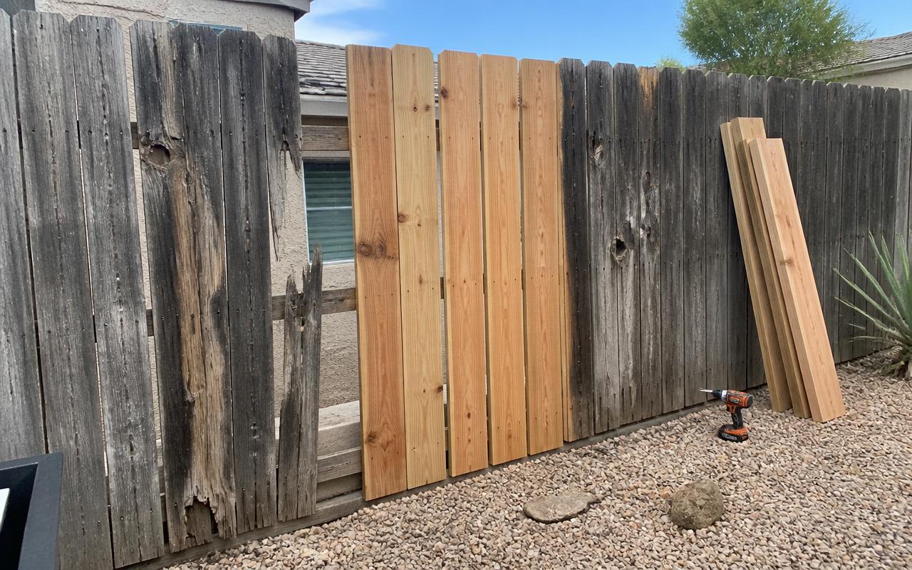 A damaged weathered wood fence in El Paso with a section being repaired using new cedar boards